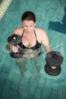 Happy pregnant woman exercising in the pool with weights