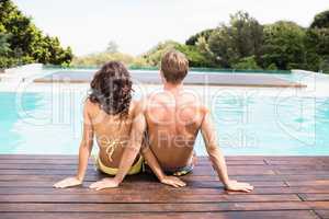 Rear view of young couple sitting by poolside