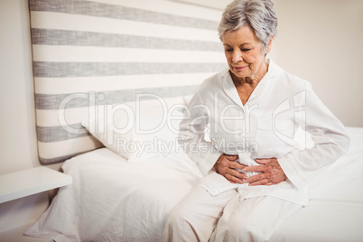 Senior woman suffering from stomach ache sitting on bed