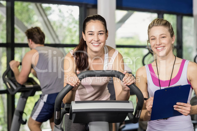 Trainer woman talking with a woman doing exercise bike