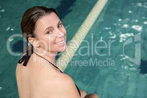 Smiling pregant woman sitting on the edge of the pool