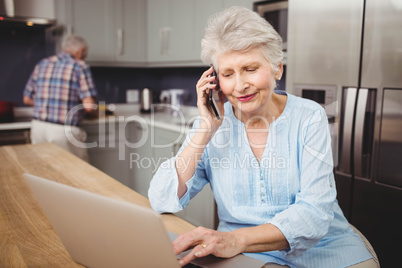 Senior woman talking on phone while using laptop and man working