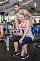 Trainer man helping woman lifting dumbbell