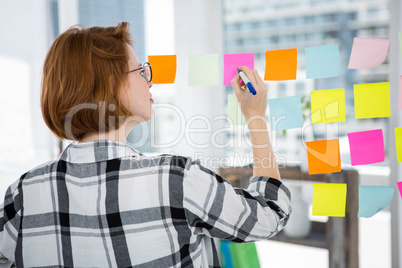 smiling hipster woman sticking notes on a notice board