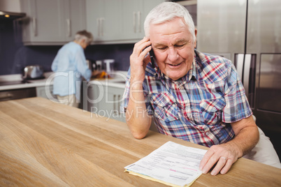 Senior man talking on phone and woman working in kitchen