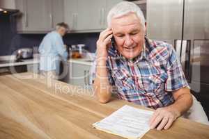 Senior man talking on phone and woman working in kitchen