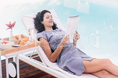 Young woman reading magazine near poolside
