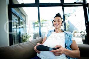 Portrait of pregnant woman listening to music on sofa