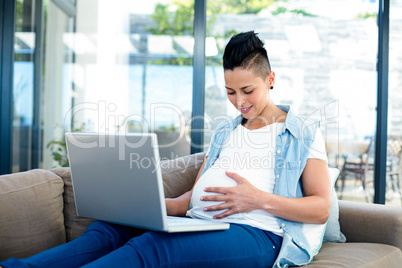 Pregnant woman relaxing on sofa with her laptop