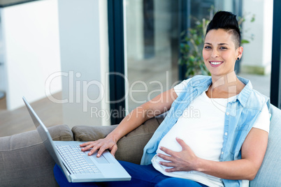 Portrait of pregnant woman relaxing on sofa with her laptop