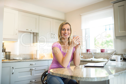 Pretty blonde woman having coffee and using laptop