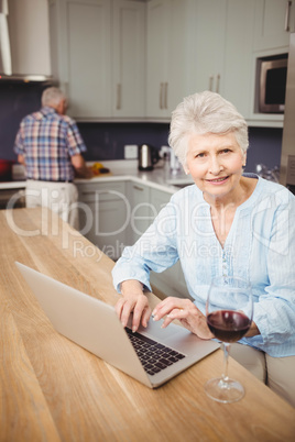 Senior woman using laptop and man working in kitchen