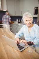 Senior woman using laptop and man working in kitchen