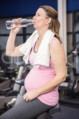 Pregnant woman on exercising bike drinking water
