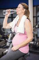Pregnant woman on exercising bike drinking water