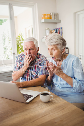 Surprised senior couple using laptop