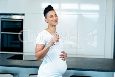 Smiling pregnant woman drinking water in kitchen