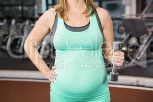 Mid section of pregnant woman holding dumbbell