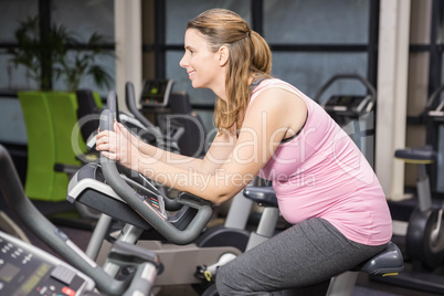 Smiling pregnant woman sitting on exercise bike