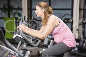 Smiling pregnant woman sitting on exercise bike