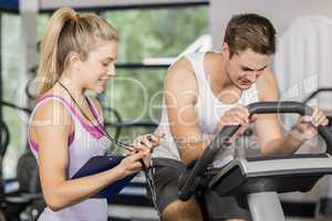 Trainer woman talking with a man doing exercise bike