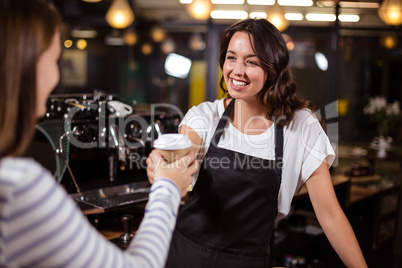 Pretty barista giving disposable cup to woman