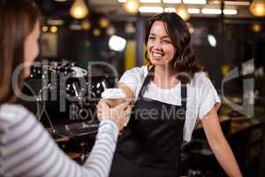 Pretty barista giving disposable cup to woman