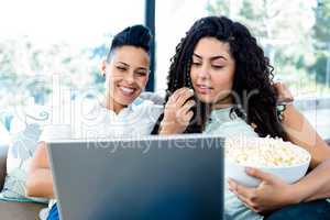 Lesbian couple having popcorn while using laptop
