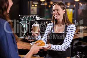 Pretty barista holding disposable cup and brioche