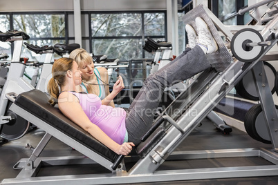 Trainer motivating pregnant woman while using leg press