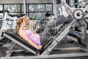 Trainer motivating pregnant woman while using leg press