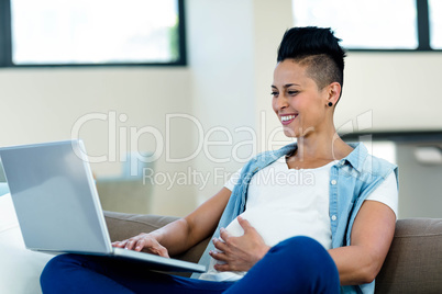 Pregnant woman relaxing on sofa with her laptop