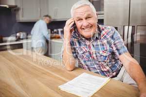 Senior man talking on phone and woman working in kitchen
