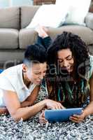 Smiling lesbian couple lying on rug and using digital tablet