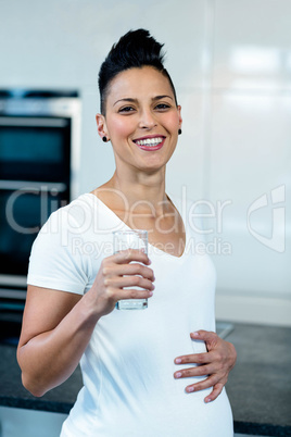 Portrait of pregnant woman drinking water in kitchen