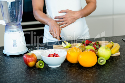 Pregnant woman touching her belly while cutting fruits