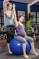 Trainer helping pregnant woman exercising on an exercise ball