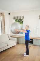 Senior woman lifting exercise ball while exercising