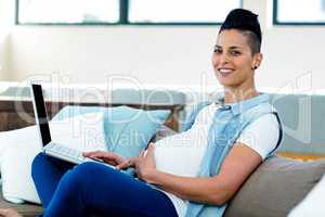 Portrait of pregnant woman relaxing on sofa with her laptop