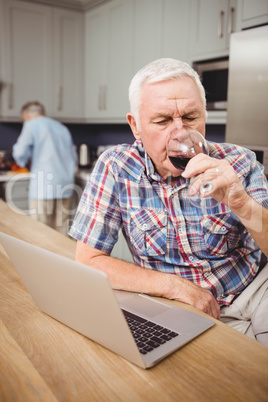 Senior man drinking red wine while using laptop