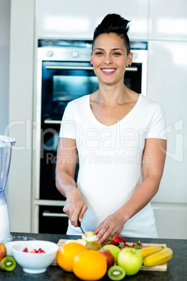 Portrait of pregnant woman cutting fruits on chopping board