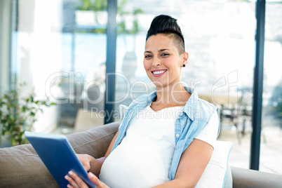 Portrait of pregnant woman relaxing on sofa with her digital tab