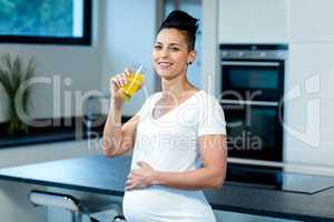 Portrait of pregnant woman drinking juice in kitchen