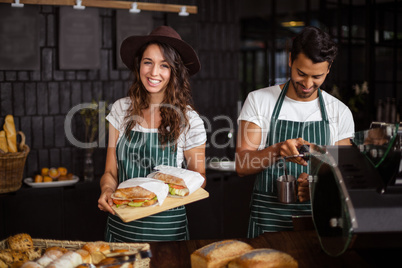 Smiling baristas holding sandwiches and making coffee