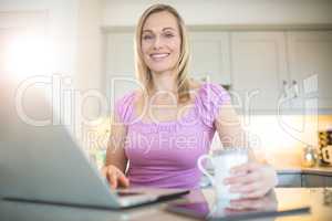 Pretty blonde woman having coffee and using laptop