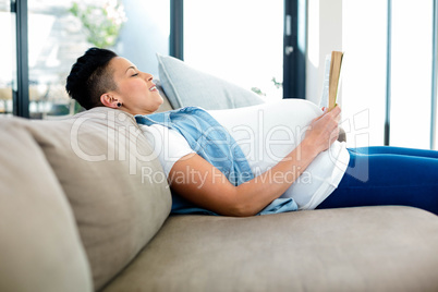 Pregnant woman reading a book while lying on sofa