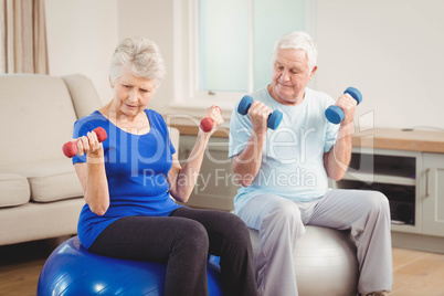 Senior couple sitting on fitness balls with dumbbells