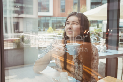 Woman looking through window with coffee
