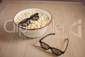 Bowl of popcorn and 3D glasses on table