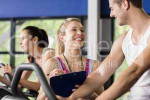 Trainer woman talking with a man doing exercise bike